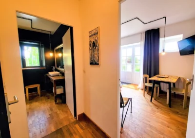 Vue d’ensemble de la salle de bain et de la chambre de Marius à La Maison Folia, avec douche à l’italienne, lavabo en bois, et coin bureau